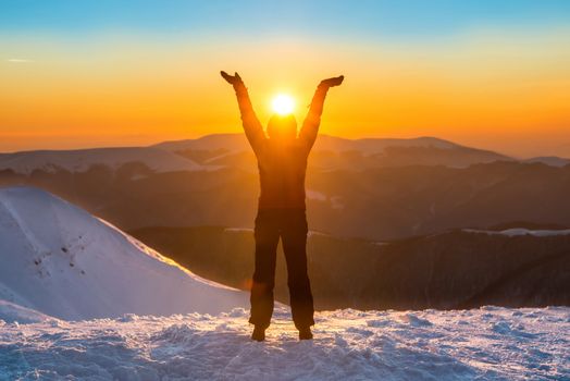 Woman on the top of winter mountain holding sun in her hands