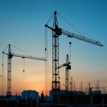 Industrial landscape with silhouettes of cranes on the sunset background