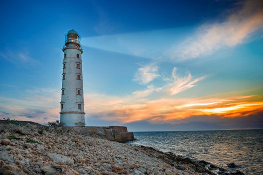 Lighthouse searchlight beam through sea air at night. Seascape at sunset