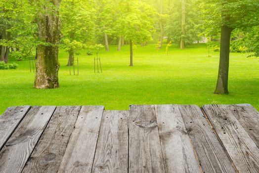 View from empty wooden deck table to the green spring foliage bokeh background