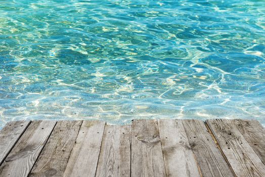 View from empty wooden deck table to tropical sunny beach with blue water background