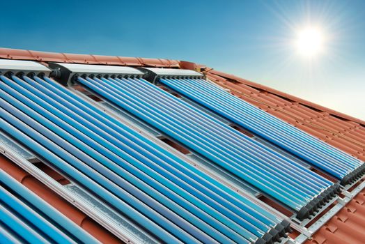 Vacuum collectors- solar water heating system on red roof of the house under shining sun and blue sky