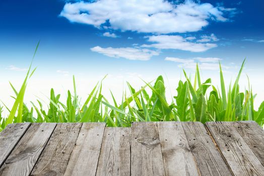 View from empty wooden deck table to the green spring grass and blue sky with clouds on background