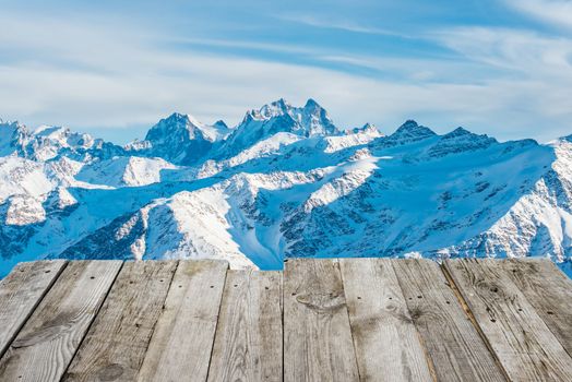 View from empty wooden deck table to the sunny winter mountains in bokeh