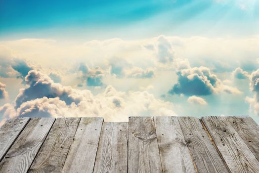 View from empty wooden deck table to the blue sky with clouds on background