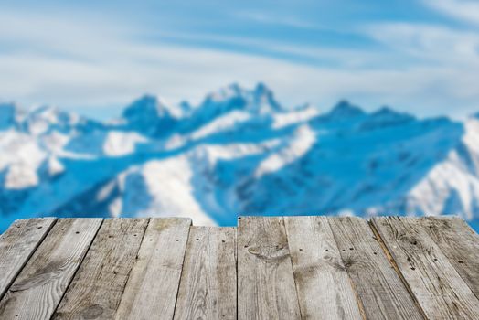 View from empty wooden deck table to the sunny winter mountains in bokeh