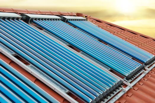 Vacuum collectors- solar water heating system on red roof of the house under shining sun