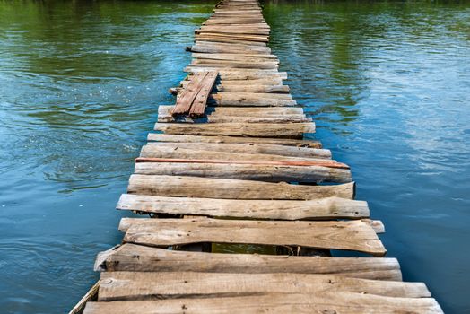 Old wooden bridge through the river with green trees on the banks