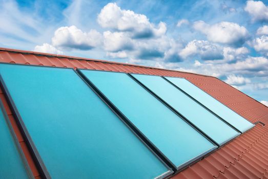Solar cells on the red house roof over blue sky with clouds
