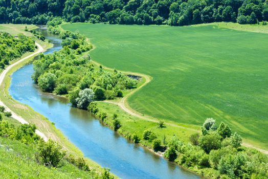 Landscape of river, green wheat field with nearby forest and country road passing by