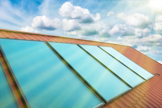 Solar cells on the red house roof under shining sun, blue sky with clouds