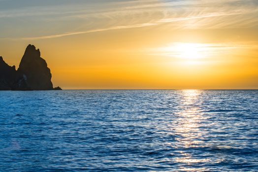 Sunset above the blue sea with rocks and orange sky