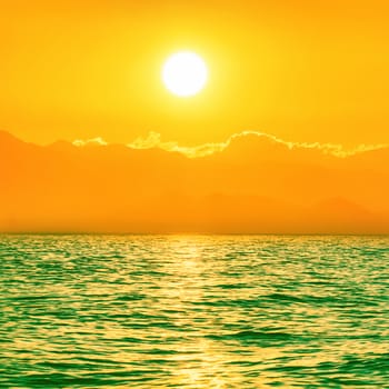 Beautiful sunset above the green sea with big shining sun and orange sky