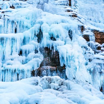 Frozen ice waterfall of blue icicles on the rock