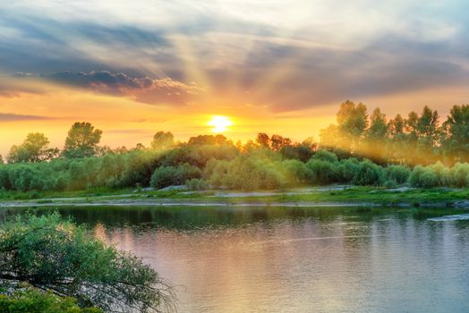 Beautiful sunset above a big river with green forest on the other coast and reflection on water