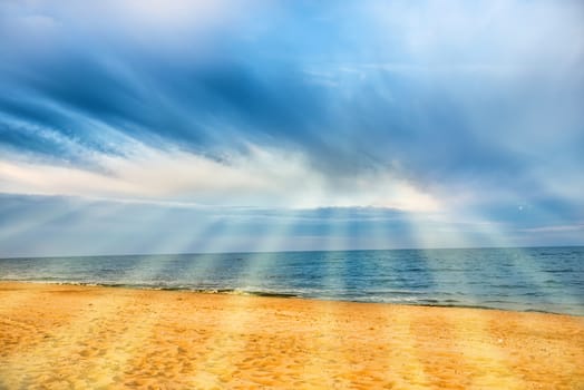 Sun shining through clouds with sunbeams above tropical beach with yellow sand and blue sea