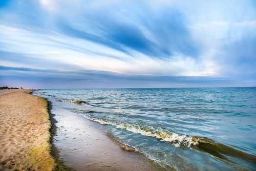 Long tropical beach with yellow sand and blue sea with waves, white clouds on background