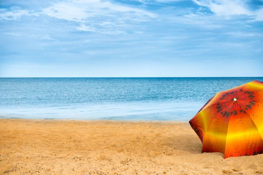 Orange umbrella on golden sand beach in a sunny day, blue sea in background