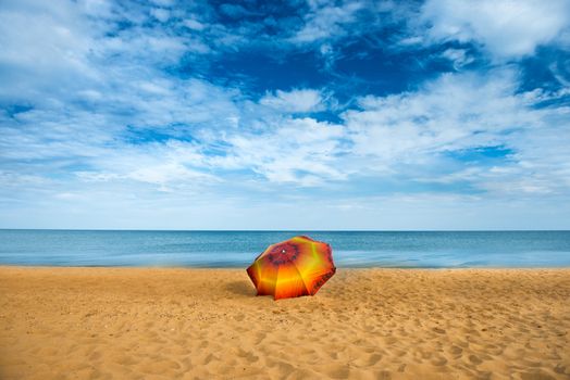 Orange umbrella on golden sand beach in a sunny day, blue sea in background