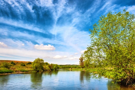 View to river banks with green trees and blue cloudy sky