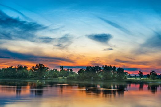 Beautiful sunset above a big river with green forest on the other coast and reflection on water