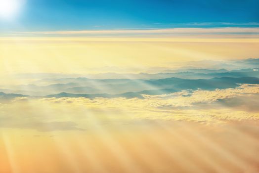 View from a plane to orange sunset on the sky with sunrays. Sunbeams shining through clouds