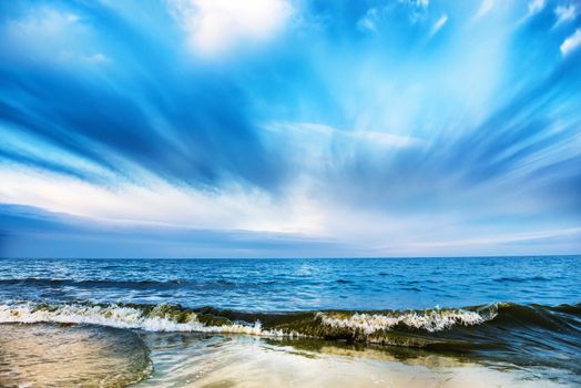 Tropical beach and blue sea with waves, white clouds on background