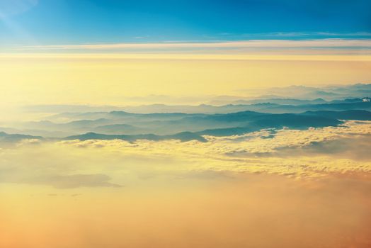 View from a plane to orange sunset on the sky with sunrays. Fluffy clouds background