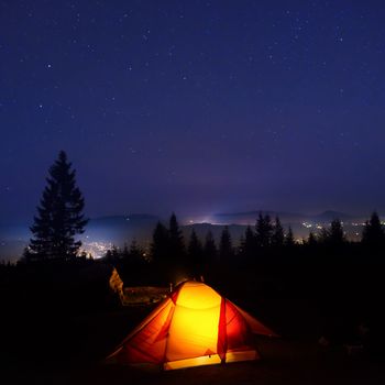 Illuminated orange camping tent under moon, stars at night