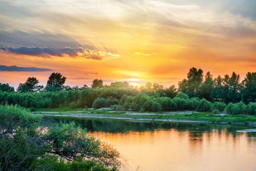 Beautiful sunset above a big river with green forest on the other coast and reflection on water