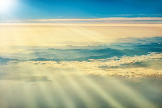 View from a plane to sunset on the sky with sunrays. Sunbeams shining through clouds