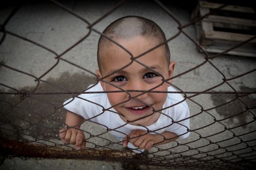 GREECE, Skaramagas: As thousands of refugees remained stranded in Greece, a boy peers through a fence at the new camp in Skaramagas, near Athens on April 14, 2016. About 1,000 refugees have found home in shipping containers here, having just been relocated from the port of Piraeus, where they were long stranded.