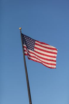 The American flag flies in the wind across a blue sky background on Independence Day in July.