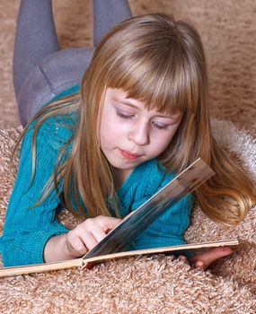 Girl 6 years old reading a book while lying on a carpet