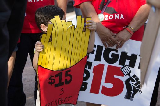 UNITED STATES, Phoenix: A child holds a sign in the shape of a cone of fries reading ' & respect' as hundreds of workers and supports took to the streets in Phoenix, Arizona on April 14, 2016 to call for a national minimum wage increase to  an hour. 