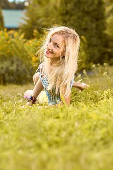 Beauty playful woman relax in summer garden smiling on grass, people, outdoors, bokeh. Attractive happy blonde girl enjoying nature, harmony on meadow, lifestyle. Sunny day, forest, flowers, copyspace