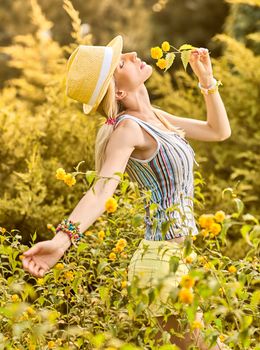 Beauty playful woman relax in summer garden dreaming, outdoors. Attractive happy blonde girl in hat with flower enjoying nature, lifestyle.