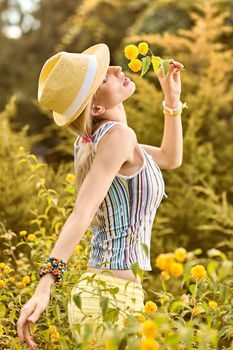 Beauty playful woman relax in summer garden dreaming, outdoors. Attractive happy blonde girl in hat with flower enjoying nature, lifestyle.