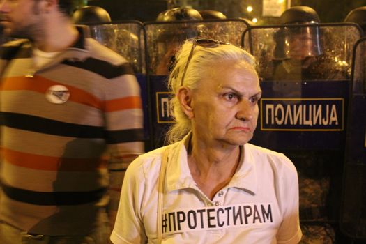 MACEDONIA, Skopje: A woman holds a placard which reads #protest, close to riot police officers, as thousands took to the streets of the Macedonian capital for a third consecutive evening to protest against the president's surprising decision to halt probes into more than 50 public figures embroiled in a wiretapping scandal in Skopje, on April 14, 2016. Similar anti-government protests in the capital had turned violent on Wednesday, when demonstrators ransacked the offices used by President Gjorge Ivanov, and set fire to the furniture.
