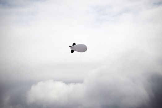 lonely single white blimp high in the grey sky
