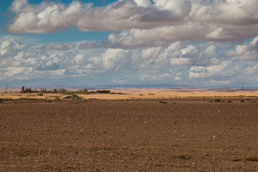 Autumn field with a light color of the dry soil. Big stormy clouds before a rain. Country close to Marrakesh.