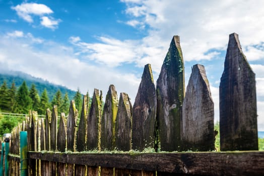 Old country fence with forest and blue sky on background