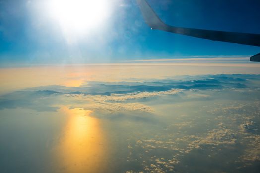 View from a plane to sunset on the sky with sunrays. Fluffy clouds background