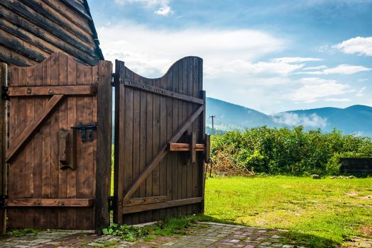 Rural wooden gate and green lawn with grass, mountains, blue sky