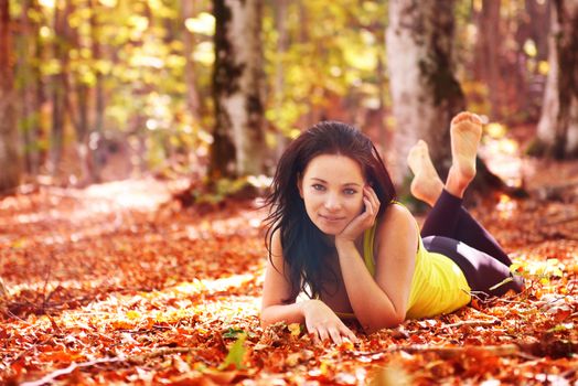 Pretty woman in the autumn forest laying on orange leaves