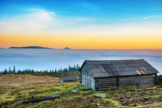 Old rural cabine in front of beautiful nature with clouds ocean, mountains and field of grass