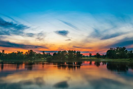 Beautiful sunset above a big river with green forest on the other coast and reflection on water