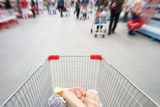 Shopping cart, trolley in a big supermarket with blurred people
