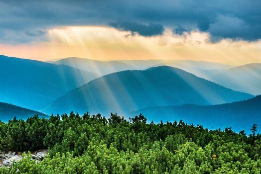 Sunset over blue mountains. Sun with sunbeams shining through the clouds