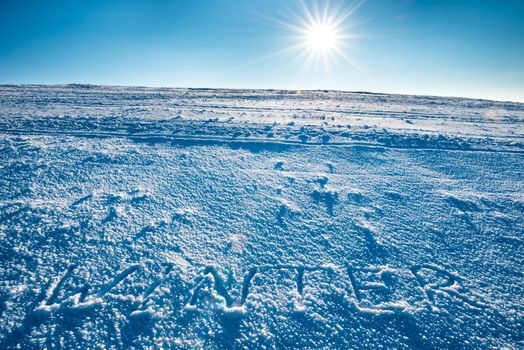 Mountain landscape with word "winter" on the snow over shining sun on bright blue sky